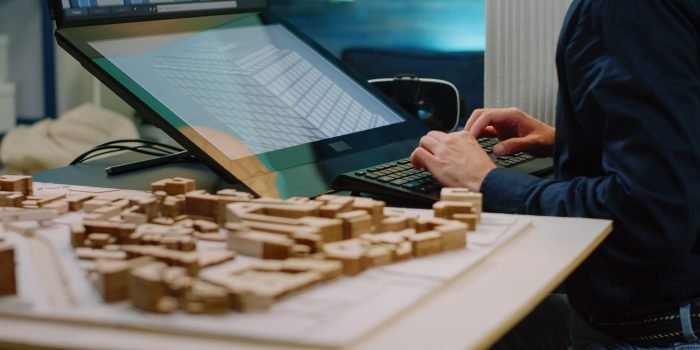 Close up of architect hands using touch screen computer and maquette on table. Man engineer working with technology to analyze building model for construction layout and development