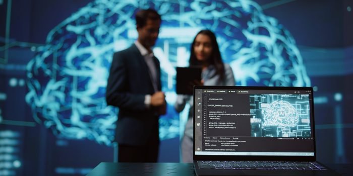 Focus on laptop in workspace used by AI researchers working with artificial intelligence in blurry background. Close up of notebook used by employees developing AI systems in tech startup, camera B
